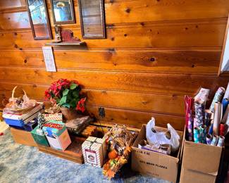 Collection of holiday decorations, gift wrapping paper, boxed decor items, and a cornucopia arranged on the floor along a wood-paneled wall.