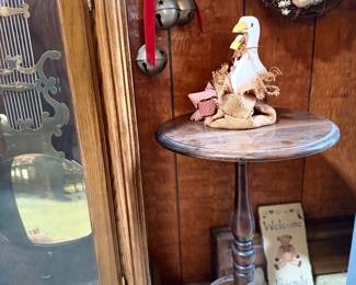 Vintage dark wood pedestal tripod side table featuring turned accents, shown alongside country-style decor items and a grandfather clock.