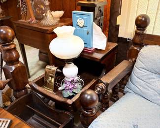 Vintage wood-frame armchair with turned finials and light blue patterned upholstery, surrounded by a rustic end table, milk glass hurricane lamp, and traditional decor.