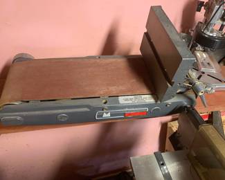 Vintage benchtop belt sander attachment featuring a cast iron frame and adjustable backstop.