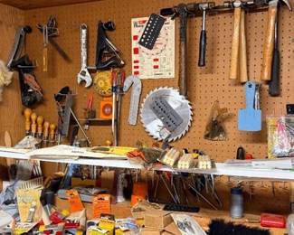 Workshop wall filled with assorted hand tools, including hammers, levels, hand planes, circular saw blades, and pegboard storage.
