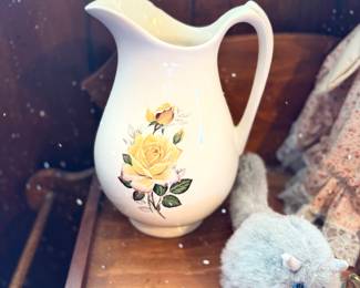 Vintage cream ceramic pitcher featuring a printed yellow rose floral motif, displayed alongside small decor items on a wooden surface.