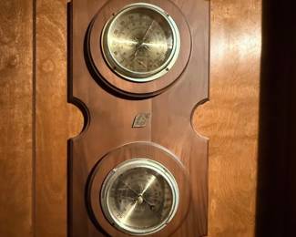 Vintage wall-mounted weather station featuring a thermometer and barometer set in a contoured wooden plaque.
