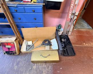 Collection of vintage tools including a Craftsman electric drill in its original box, a metal toolbox, and power tool accessories arranged on a workshop floor.