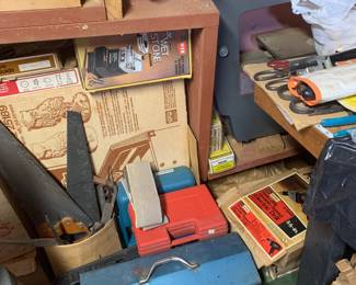 Workshop corner packed with woodworking tools, including a ShopSmith band saw, vintage hand saws, toolboxes, and boxed power tools.