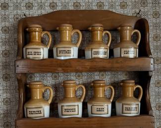 two-tier vintage wooden spice rack holding an 8-piece set of cream and tan ceramic jug-style spice jars with matching lids and printed labels