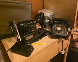 estate sale. Vintage black Singer sewing machine with foot pedal and a classic rotary dial telephone, great for collectors or vintage décor. Keywords: Singer sewing machine, antique, rotary phone, mid-century, collectibles.