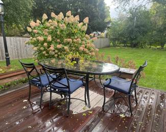 Four black aluminum patio dining chairs and dining table. Three have blue cushions; one has a beige cushion