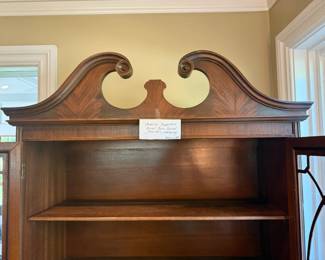 American Chippendale revival china cabinet from the 1930s or 1940s. Broken swan-neck pedimenand flame mahogany veneer on lower doors; oval brass pulls and decorative glazing.