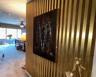 Gold-striped accent wall with framed art and brass sconce