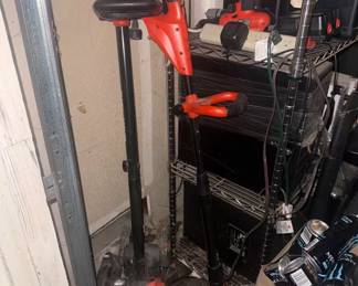 outdoor power tools and garage equipment setup. Includes a reliable Black & Decker corded electric string trimmer/lawn edger, a companion lawn tool attachment, and an orange Black & Decker cordless drill/driver. Perfect bundle for home lawn maintenance and quick DIY projects
