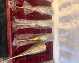 A stunning vintage hospitality set featuring 6 metal champagne flutes. Each glass has a beautifully textured, ribbed silver-tone body paired with a sleek gold-tone stem and base. The set comes protected in its original, luxurious deep red velvet presentation display box with a clean satin-lined interior lid. Most glasses are still individually wrapped in plastic