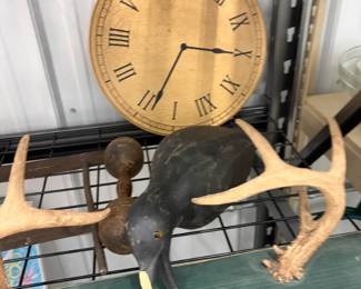 Wall clock, antlers, and carved duck decoy.