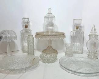Clear Glass Cake Stand, Apothecary Jars, Decanters and Serving Trays - A pressed glass cake stand, two lidded apothecary jars, two decanters with cork stoppers, a candle lamp, bud vases, and two serving trays. A useful lot for entertaining.