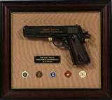 Lot#215, "JOHN WAYNE ARMED FORCES COMMEMORATIVE, 1911 COLT SEMI-AUTOMATIC PISTOL, NON-FIRING, ON FRAMED PLAQUE, L 5" BARREL,consists of a NON - FIRING replica of a Colt Model 1911 semi-automatic pistol in a shadow box frame. Gilt engraving on slide inscribed: "John Wayne Armed Forces Commemorative"; brass plate inscribed: "The John Wayne Commemorative .45 Automatic", lower left. Mounted on framed plaque;  FOR DISPLAY ONLY; NON-FIRING REPLICA PISTOL, DOES NOT FIRE ANY AMMUNITION, GA.
