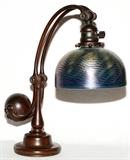 Lot#1073, TIFFANY STUDIOS BRONZE & DAMASCENE GLASS COUNTER BALANCE DESK LAMP, EARLY 20TH C., H 15", DIA 7 7/8"Bronze counter balance lamp base stamped "Tiffany Studios, New York, 417" underneath, fitted with a blue Damascene glass shade, signed "L. C. T. Favrile" at the fitter rim (see additional photos).