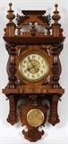 Lot#1497, GERMAN WALNUT WALL CLOCK, C. 1880, H 35", W 15"Spring movement, fancy crest, pressed metal dial and pendulum.
