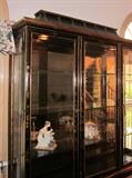 Oriental black lacquer china/curio cabinet from Plunketts.  Decorated with oriental scenes, flowers, foliage, etc.  Six beveled glass door, glass shelves, top and bottom section individually lighted.  Separates into two pieces.