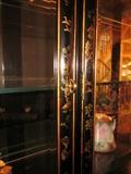 Oriental black lacquer china/curio cabinet from Plunketts.  Decorated with oriental scenes, flowers, foliage, etc.  Six beveled glass door, glass shelves, top and bottom section individually lighted.  Separates into two pieces.