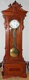 Lot#137, GILBERT #8 STANDING GRANDFATHER CLOCK, H 104", W 33", D 13"PORCELAIN FACE. CHERRY WITH MAHOGANY FINISH. REGULATOR #8. CARVED CASE ELABORATELY DESIGNED WITH FINE CABINET FINISH. GLASS SIDES. FITTED WITH 8 DAY WEIGHT MOVEMENT,DEAD BEAT ESCAPEMENT AND RETAINING POWER. GRID IRON PENDULUM. DuMouchelles does not guarantee working order or original parts for clocks and watches.