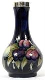 Lot#1005, MOORCROFT POTTERY CABINET VASE WITH SILVERPLATE RIM, C. 1925, H 6 1/2"Decorated with a plum and leaf motif on a dark blue ground, having a silverplate rim made by William Hutton & Sons; impressed "Moorcroft, Made in England" with signature in green under glaze (see additional photo).