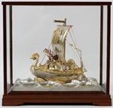 Lot#1162, JAPANESE STERLING & GILT TAKARA BUNE TREASURE SHIP, W 8"Japanese Sterling silver Takehiko treasure ship of the Immortals. Approximately 215 gms of silver. 7 3/4" H. x 7 3/4" L. includes a glass panel case with bracket feet, 18" H. x 18" L. all enclosed in a wood hinged storage box which is signed and inscribed on inside of hinged door in Japanese script and red block signature.