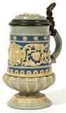 Lot#1288, VILLEROY & BOCH, METTLACH STEIN, H 6 1/4", DIA 3 3/4"A 1/4 liter size stein with pewter rim and thumb lift, impressed number 1184. Tan relief or applied designs on the blue banded lid and body, pedestal base.