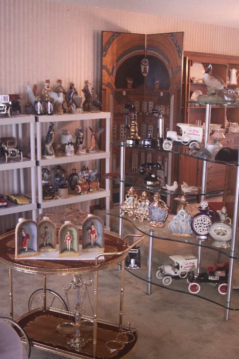 Living room full of vintage decanters, collectibles, vintage Italian wood inlay tea cart, glass shelving unit and more