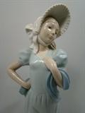 Lladro Girl with Bonnet Porcelain Figurine. Girl still has an inspection sticker on her back. Measures 13"h. and is in Excellent Condition. 