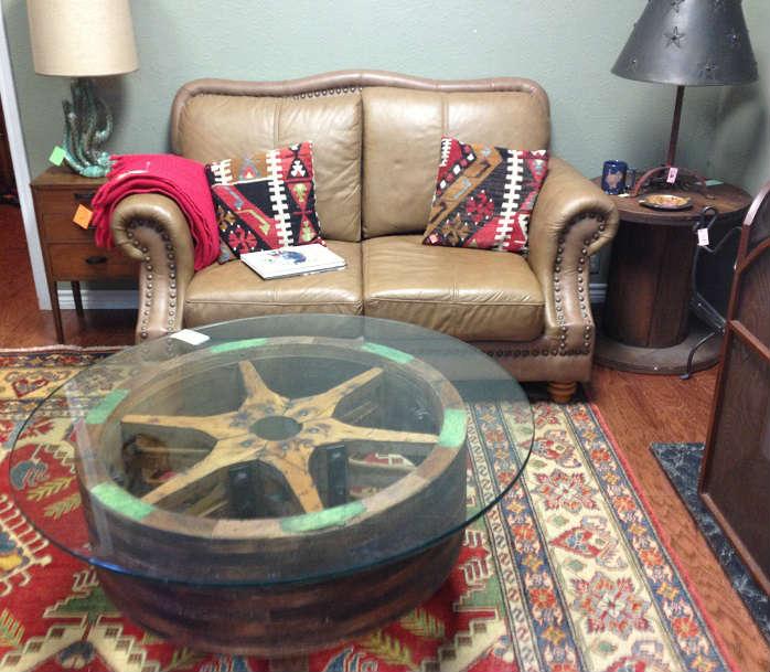 Wooden grinding wheel coffee table with glass top, kilim rug and pillows, leather loveseat, metal lamp, vintage cactus lamp.