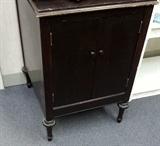 Dark stained solid wood small cabinet with doors on front for storage.