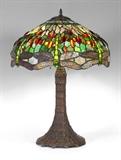 Lot 1076:  TIFFANY STYLE DRAGONFLY TABLE LAMP: Based on the classic Tiffany ''Dragonfly shade'', patinated cast metal base. 3 socket fixture. Multi-hued stained glass shade with dragonfly design. Base 28 1/4'' h. x 11 1/2'', shade 10'' h. x 21 1/4'' dia.