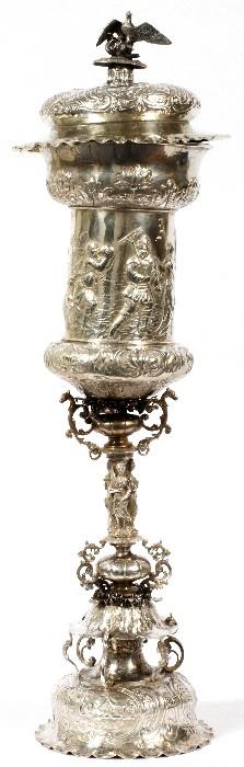 Lot#1001, GERMAN SILVER PRESENTATION COVERED CUP, 19TH C., H 25", DIA 7"A 19th century silver goblet form cup having dome cover with bird finial. Classical frieze decorates cup itself which rests on caryatid cluster of three maidens. Tiered base.  Hallmarks on cover and foot, including "13", indicating .812 fineness (see additional photo).  Eagle finial. Underside of cover is gold plated. Weighs approximately 54.4 troy oz.