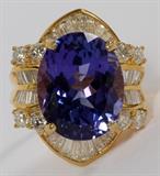 Lot#1065, UGL 18KT GOLD, 14.26CT BLUE TANZANITE & DIAMOND COCKTAIL RING, 13.4GR,18 kt yellow gold ring, featuring a 14.26 carat oval natural blue tanzanite, surrounded by round brilliant and baguette cut side diamonds, measuring 2.30 carats in total weight, with a G-color, VS-2 clarity grading. The total weight of the ring is approximately 13.4 grams. Size 6.5.