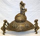 Lot#10, AFRICAN BRONZE FIGURAL COVERED POT, H 26", L 31"Rounded diamond form pot, raised by figures at either side, decorated with a stylized geometric border, and a grouping of three figures in relief at each end. The pot has a bulbous form opening at the top, with a Royal figure finial. Measures H. 26" x 31". Property from the Henry Stallings II Collection, Detroit, MI.