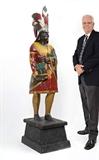 Lot 1012:  ROBB, Samuel Anderson, (American, 1851-1928): Attribution, polychrome paint decorated cigar store Indian. Tradition has it this Indian was purchased many years ago from a store less than 4 block from Robb's New York Studio, unfortunately the name of the store has been lost. This carving exhibits many traits similar to Robb's style, base is a replacement. Indian measures 58 1/2'' h. x 14'' x 16'', base 13 3/4'' h. x 22 1/4'' x 17 1/2''. Est. $15000/20000**
CONDITION: Flaking and loss of paint, several age splits.