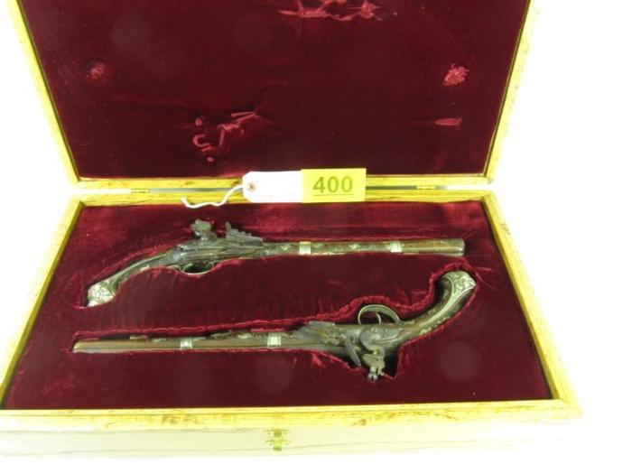 Lot#:	400
Description:	Firearm 1700's British Flintlock Dueling Pistols
This lot includes two beautiful Flintlock Dueling Pistols with a custom wooden display case. According to paperwork that goes along with these pistols they are British from the years between 1730-1739. The letter goes on to say that they may have been for an individual military officer or the nobility (in the Kings Commission). The pistols themselves are wonderfully crafted with metal inlayed throughout. Condition varies between the two, Pistol one has a crack in the wood under the barrel lengthwise, a couple of chips in the wood, and some loose components. Pistol two has a loose trigger guard as a result of some cracks in the wood near the receiver, chip and crack near muzzle, and loose components. Both have some light rust/pitting on barrels and missing ram rods. For being estimated from the 1700's they have stood the test of time. They have not been test fired.
Tag Words: Gun, Antique, Collectible, Rare
NO ADDIT