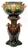 Lot#1349, MAJOLICA MAJOLICA POTTERY JARDINIÈRE & PEDESTAL, C. 1900, H 12", 21", LION HEADS.Pottery jardinière is 12" high and 14" in diameter. Width to lion handles is 20". Circa 1900. Probably American.