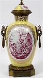Lot#1351, AUGUSTUS REX PORCELAIN COVERED URN, MOUNTED AS A LAMP, H 36 1/2"Having a yellow ground, with putti scene decoration in magenta, encircled by finely detailed gold gilt borders. Two hanging brass loop handles at either side, with brass trim along base and lid, all having grape vine motif decoration.  Marked in blue underglaze (see additional photo).