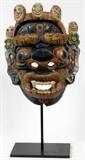 Lot#295, BALINESE CARVED POLYCHROME DEMON DANCE MASK, H 15"Carved wood oval hollow form mask, with protruding, elongated ears, featuring an open fanged mouth with wide-set googly eyes. Decorated in blue with gilt leaves in relief at either side of the mouth, shows a third eye on the forehead. The mask is adorned with a headdress, lined by raised smiling face decoration.
