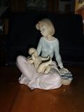 A piece by Lladro entitled "Mother and Child" in hand painted porcelain. It shows a seated mother with child on her lap and laundry by her side in a basket. This piece stands 6" by 7.5" high.