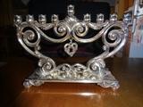 A silver plated iron Menorah with a hanging heart in the center, and standing 10" wide by 7" high.