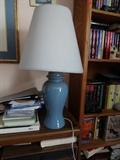 A blue ceramic lacquered lamp that is 28" high with a 5" diameter stand. It has a white lamp shade.