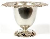 Lot#1009, REED & BARTON STERLING VASE, C. 1920, H 8", DIA 11 1/2"Urn-form sterling silver vessel with evert rim pierced with a scroll and floral medallion motif, raised on a coordinating domed base, stamped at the underside with trademark and number 294.
