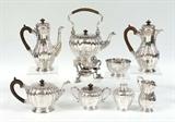 Lot 1002:  CRICHTON BROTHERS 8 PIECE ENGLISH SILVER TEA SERVICE: Circa 1912-13, embossed and engraved foliate motifs on each piece by Crichton Brothers, New York and London to include 1) Hot water kettle on stand with burner, hinged lid, articulated handle with wood. 10 1/2'' h. x 10''. 2) Coffee pot, hinged lid, wood handle, 10 3/4'' h. x 9''. 3) Chocolate pot, hinged lid, wood handle, 10 1/4'' x 8''. 4) Tea pot with hinged lid, wood handle, 6'' h. x 11 1/4''. 5) Open creamer, 6'' h. 6) Covered sugar, 5'' h. x 7 1/2''. 7) Covered tea caddy, 5'' h. x 4''. 8) Open waste bowl, 3'' h. x 5 1/4''. Each piece monogrammed. Approx. 207.4 troy oz inclusive of wood handles and finials. Estate of Elton Hoyt II
CONDITION: Minor signs of use.