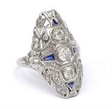Lot 1029:  PLATINUM ART DECO 3 DIAMOND FILIGREE RING: Platinum filigree ring contains 3 old European round cut diamonds and 14 round single cut diamonds totaling approx. 1.00 Ct. Approx. Rated SI in clarity and H-I in color. The 4 sapphires are synthetic. Weight: 5.2 grams. Size: 8 Est. $1250/1600**