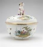 Lot# 1004 A Berlin style porcelain punch bowl & cover Late 19th / early 20th century, with under-glaze blue scepter mark, the finial modeled as a kneeling Bacchic putto holding a wine flask and raising a goblet, the circular bowl and domed cover with ozier-molded bands and polychrome-painted with butterflies and scenes of fowl in landscapes, with gilt foliate rim borders, 13.5'' H x 11'' Dia., est: $700/900