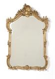 Lot# 1021 A carved gilt wood wall mirror Early 20th century, the arched beveled glass plate within a C-scroll, floral, foliate and rocaille-decorated crested surround, 48'' H x 32.5'' W x 5'' D, est: $600/900