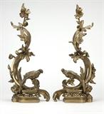 Lot# 1023 A pair of Rococo style gilt bronze chenets Late 19th / early 20th century, each modeled with a bird perched atop scrolling foliage intertwined with a flower stalk, on a pierced rocaille base, 2 pcs, each 26'' H x 10.5'' W x 7.5'' D, est: $800/1200