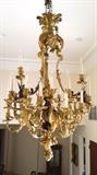 Lot# 1024 A French gilt & patinated bronze twenty-four light chandelier First quarter 20th century, of Louis XV style, suspended from a cluster of plumes surmounting the tripartite, scrolling rocaille and acanthus-cast frame, each downswept branch capped with a fully modeled figure of a dragon topped with a foliate candlearm and continuing downwards to a relief-cast espagnolette issuing two bifurcated scrolling foliate candlearms, surrounding the spiral-cast baluster-form stem with flambeau finial issuing three sets of trifurcated candlearms, electrified, 56'' H x 36'' Dia., est: $15,000/20,000